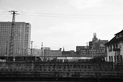 Low angle view of electricity pylon and buildings against sky on sunny day