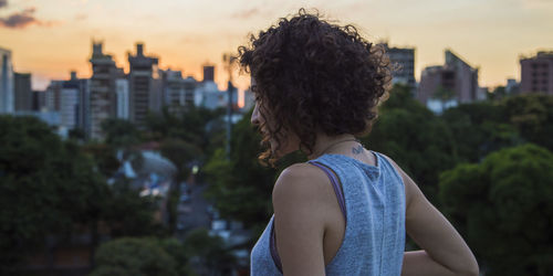 Rear view of young woman standing in city during sunset