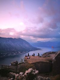 People on sea by mountains against sky during sunset