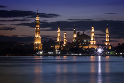 Illuminated mosque by river against sky at night