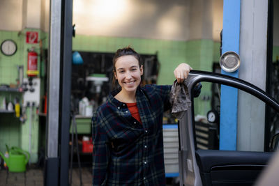 Smiling female mechanic opening car door at workshop