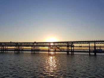 Pier over sea against clear sky during sunset