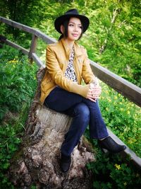 Beautiful young woman sitting on tree stump in forest