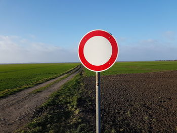 Road sign on field against sky