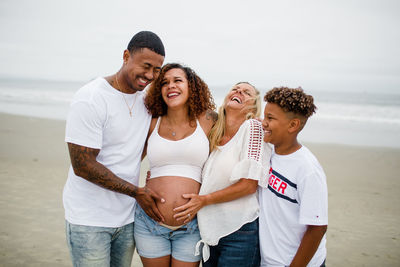 Family posing & laughing for maternity photos on beach