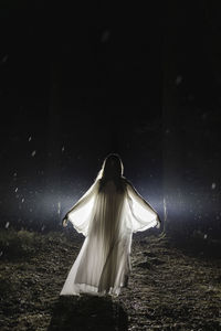 Ghost with arms outstretched standing in forest at night during rainy season