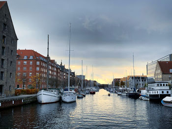Sailboats moored on canal amidst buildings in city against sky