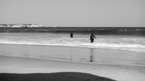 Silhouette people on beach against clear sky