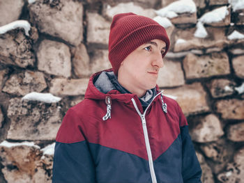 Portrait of man wearing hat standing against stone wall