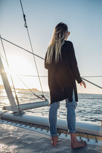 Rear view of woman standing on railing against sea