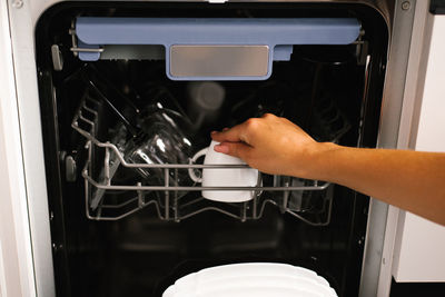 A woman loads dishes into the built-in dishwasher cups, glasses, plates. type of hand and dishes