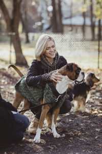 Smiling blond woman crouching by friend with dogs at park