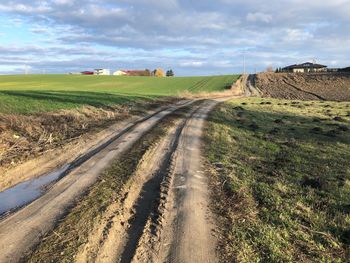 Dirt road amidst field against sky