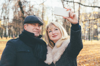Smiling mature couple taking selfie at park during autumn