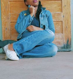 Low section of young woman sitting by wooden door