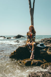 Portrait of woman sitting on rock by sea against clear sky