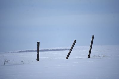 Wooden posts on snow covered field against sky