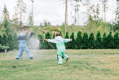 Sister spraying her brother with water whilst playing outside in rain