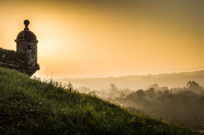 Lookout tower of fort on grassy hill against clear sky during sunset