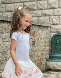 Girl standing against wall smiling in a blue dress long blond hair 