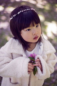 Korean girl in a white light fur coat and a headband stands in a garden with cherry blossoms