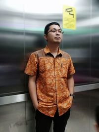 Young man looking away while standing against wall