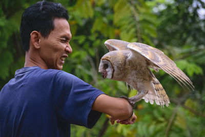 Mid adult man holding owl while standing against clear sky