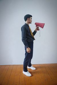 Young man looking away while standing on hardwood floor against wall