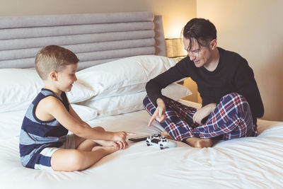 Father and son playing while sitting on bed at home