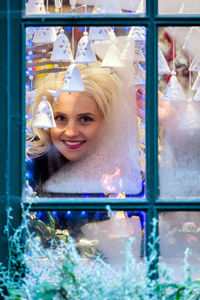 Portrait of smiling young woman standing by glass window