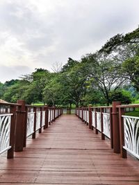 Footbridge along plants and trees against sky