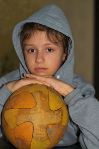 A girl in a gray hoodie with a hood is holding a ball.