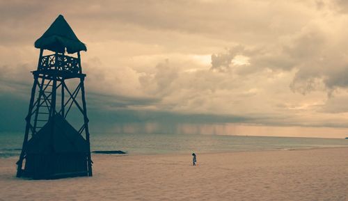 Lookout tower at sea shore against cloudy sky during sunset