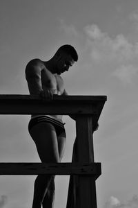 Low angle view of shirtless mature body builder standing on balcony against sky