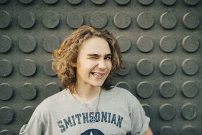 Portrait of smiling young man winking against wall