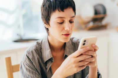 Close-up of a young woman with a short haircut is using a mobile phone to surf social networks.