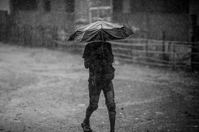 Man with umbrella walking on road during monsoon