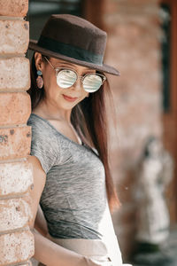 Portrait of young woman wearing hat against wall