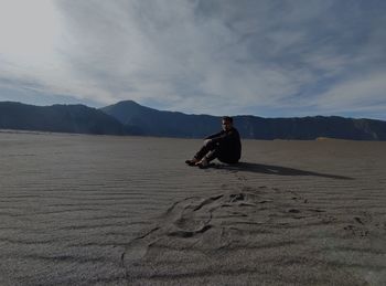 Rear view of man sitting on beach against sky