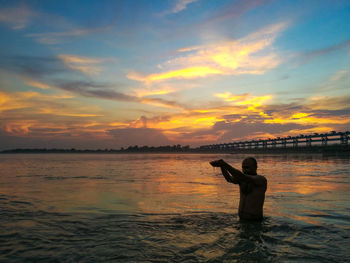 Man standing in sea against sky during sunset