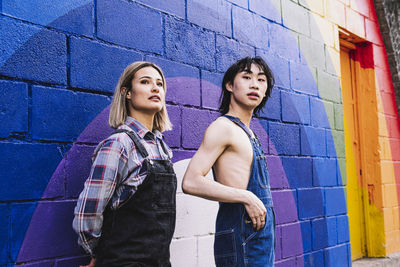 Young woman standing by man in front of rainbow painted on wall