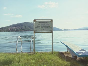 Information sign by sea against sky