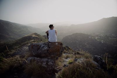 Man standing on rock looking at mountain against sky