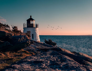 Lighthouse by sea against sky during sunset