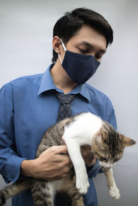 Portrait of doctor wearing mask holding cat against wall