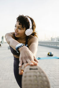 Athlete with headphones stretching while exercising on footpath