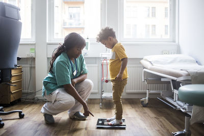 Mature doctor pointing while boy standing on weighing scale in clinic