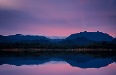 Scenic view of lake by silhouette mountains against romantic sky