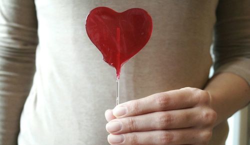 Mid section view of woman holding heart shape lollipop