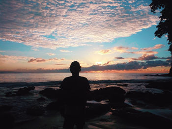 Silhouette man looking at sea against sky during sunset